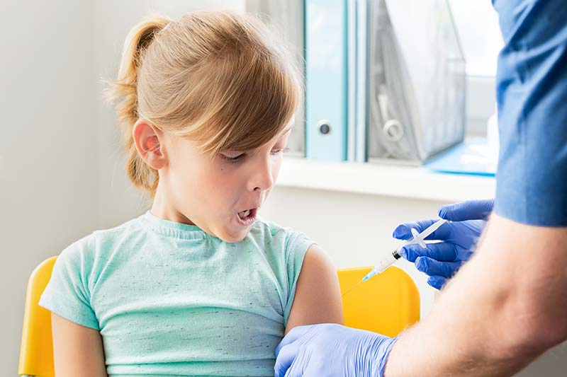 A young child smiling while receiving a flu vaccine from a healthcare professional.