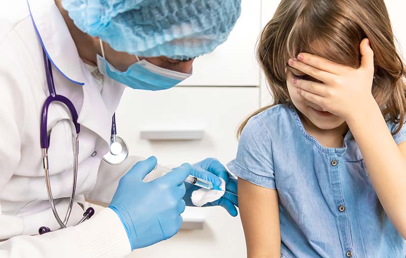 Child receiving the COVID-19 vaccine with a smiling nurse in a pediatric clinic.