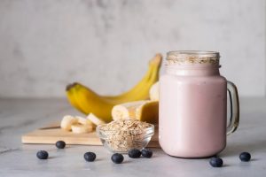 A nutritious protein shake in a glass with fresh fruits and protein powder.